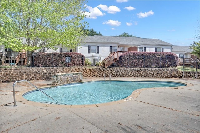 community pool with fence, a patio, and stairway