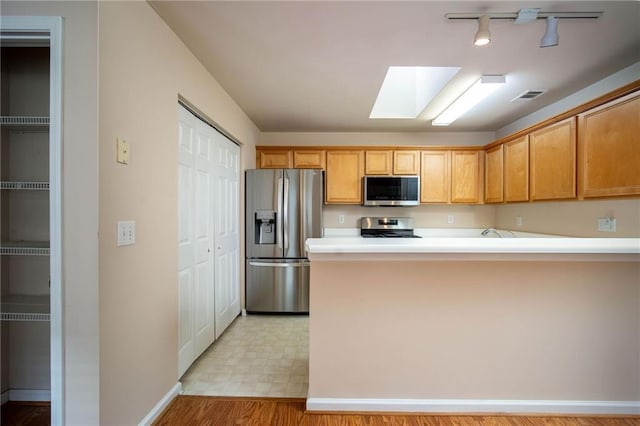 kitchen with kitchen peninsula, appliances with stainless steel finishes, and a skylight