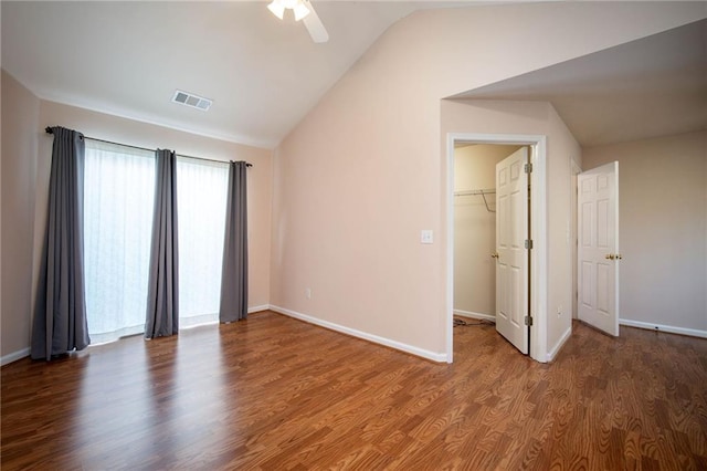 unfurnished bedroom with ceiling fan, a spacious closet, vaulted ceiling, a closet, and hardwood / wood-style flooring