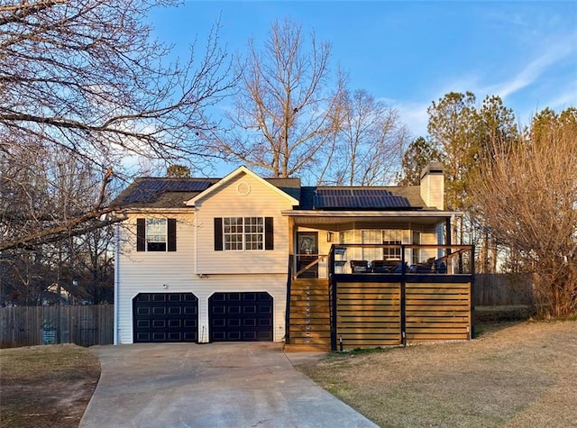 view of front of home with an attached garage, solar panels, fence, driveway, and a chimney