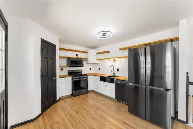 kitchen featuring a sink, black dishwasher, freestanding refrigerator, open shelves, and gas stove