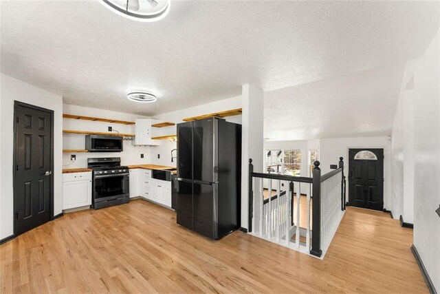 kitchen featuring open shelves, stainless steel microwave, gas stove, freestanding refrigerator, and white cabinetry