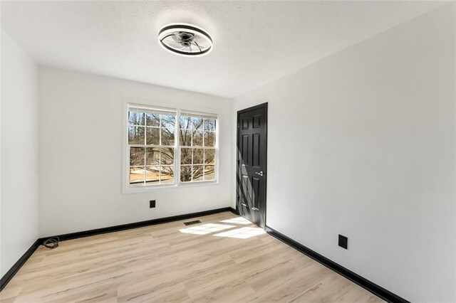 spare room featuring light wood-style floors, visible vents, and baseboards