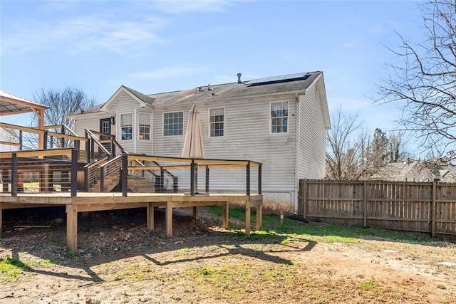 rear view of house featuring a deck, solar panels, and fence