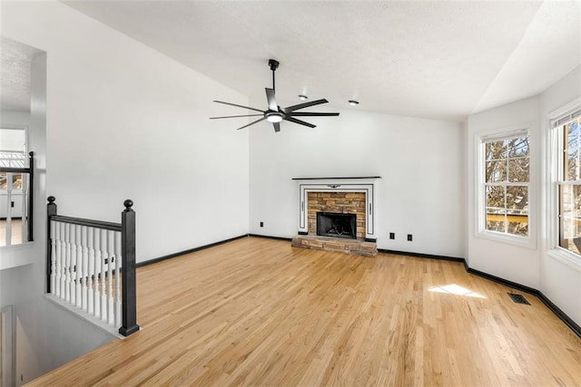 unfurnished living room with a fireplace, visible vents, light wood-style floors, vaulted ceiling, and baseboards