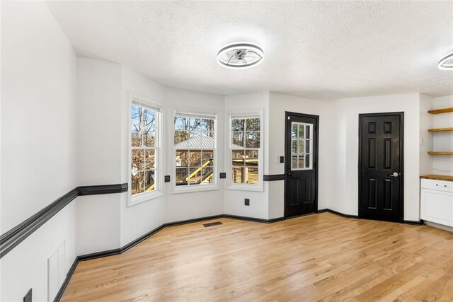 unfurnished dining area featuring light wood-type flooring, visible vents, a textured ceiling, and baseboards