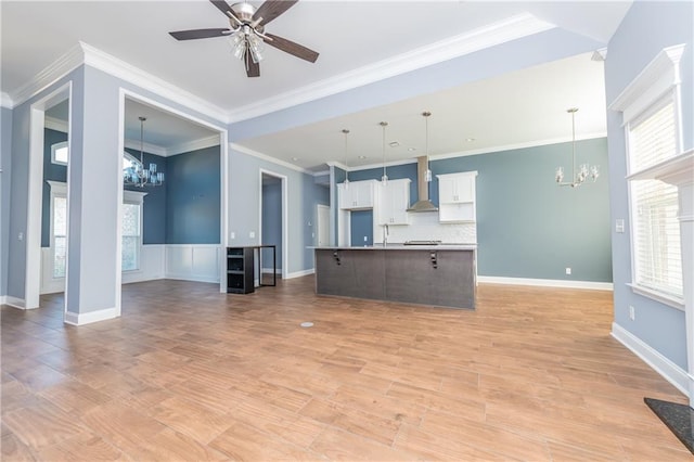 unfurnished living room with crown molding, ceiling fan with notable chandelier, a healthy amount of sunlight, and light wood-type flooring