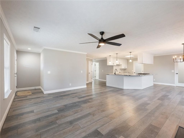 unfurnished living room with ornamental molding, ceiling fan with notable chandelier, and dark wood-type flooring