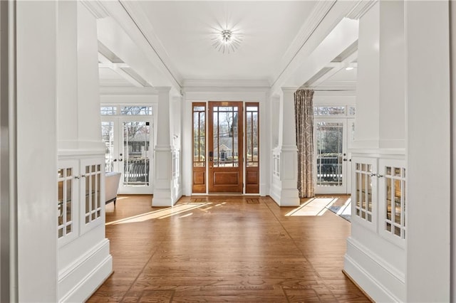 foyer with crown molding, french doors, wood finished floors, a decorative wall, and ornate columns