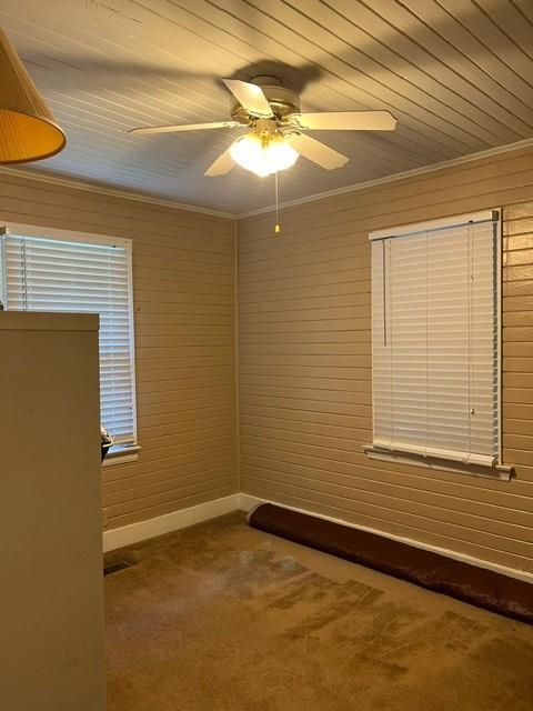 spare room with ornamental molding, wooden walls, carpet flooring, and ceiling fan