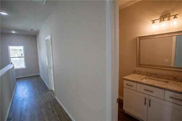 hallway with a sink, wood finished floors, attic access, and baseboards