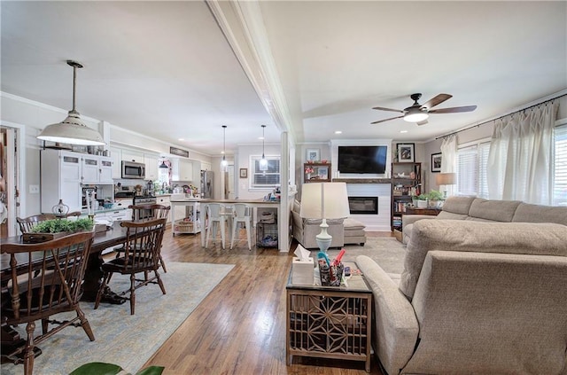 living room featuring a ceiling fan, light wood-style flooring, recessed lighting, ornamental molding, and a glass covered fireplace