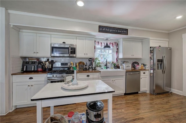 kitchen featuring a sink, wood finished floors, white cabinetry, appliances with stainless steel finishes, and crown molding