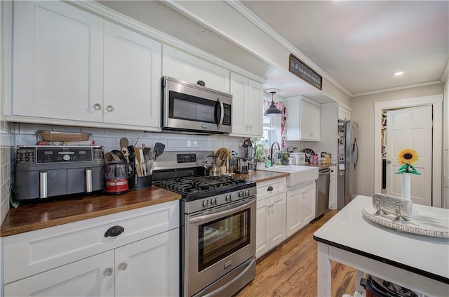 kitchen featuring a sink, tasteful backsplash, stainless steel appliances, white cabinets, and crown molding