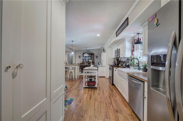 kitchen with light wood finished floors, tasteful backsplash, stainless steel appliances, white cabinetry, and a sink