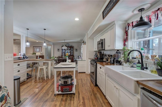 kitchen featuring tasteful backsplash, stainless steel appliances, wood finished floors, white cabinetry, and a sink