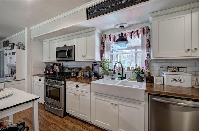 kitchen with a sink, stainless steel appliances, butcher block countertops, and crown molding