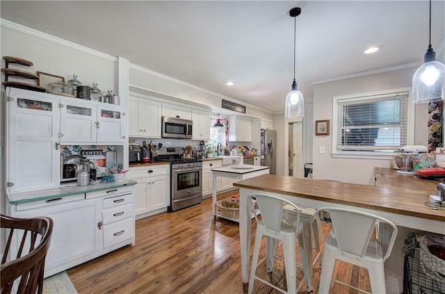 kitchen with crown molding, decorative light fixtures, wood finished floors, white cabinets, and stainless steel appliances