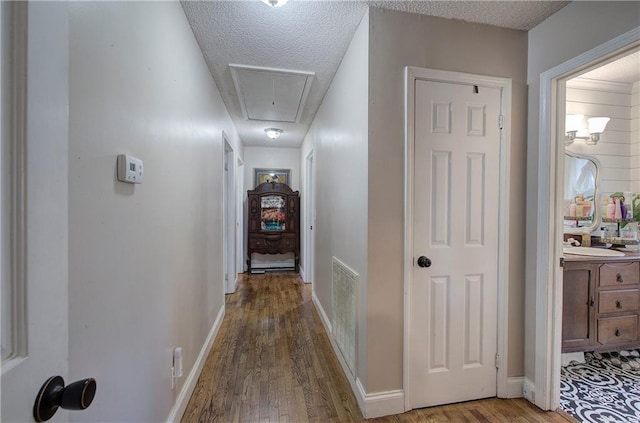 hallway with visible vents, a textured ceiling, attic access, and wood finished floors