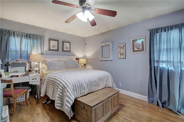 bedroom featuring light wood-type flooring, baseboards, a textured ceiling, and a ceiling fan