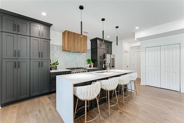 kitchen with pendant lighting, backsplash, a center island with sink, sink, and light hardwood / wood-style flooring