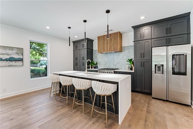 kitchen with a kitchen island with sink, hanging light fixtures, light hardwood / wood-style flooring, a breakfast bar area, and stainless steel appliances