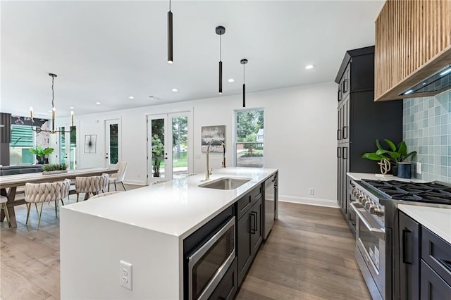 kitchen featuring a kitchen island with sink, sink, hanging light fixtures, decorative backsplash, and stainless steel appliances