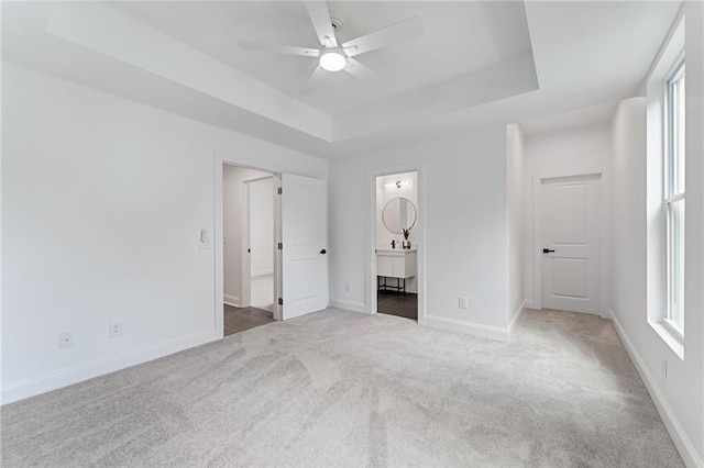 unfurnished bedroom featuring carpet, ceiling fan, connected bathroom, and a tray ceiling