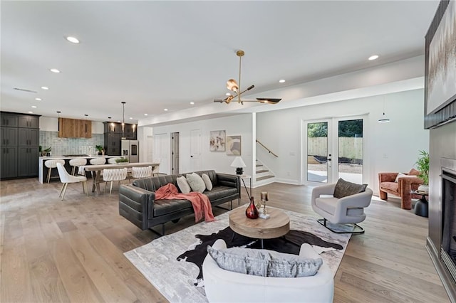 living room with a fireplace, french doors, light wood-type flooring, and a notable chandelier