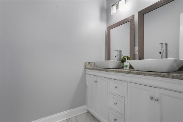 full bathroom with double vanity, marble finish floor, baseboards, and a sink