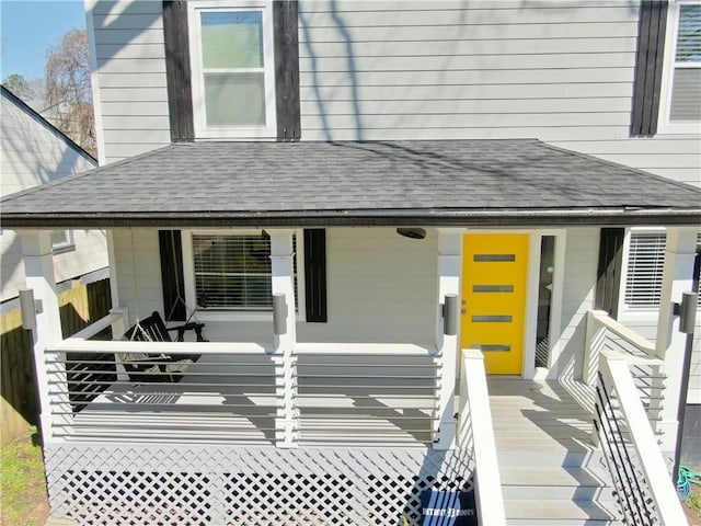 exterior space with covered porch, a shingled roof, and fence