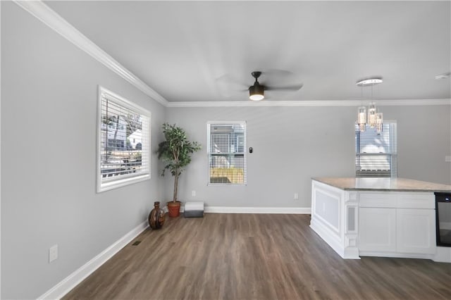 interior space with dark wood-type flooring, ceiling fan with notable chandelier, baseboards, and ornamental molding