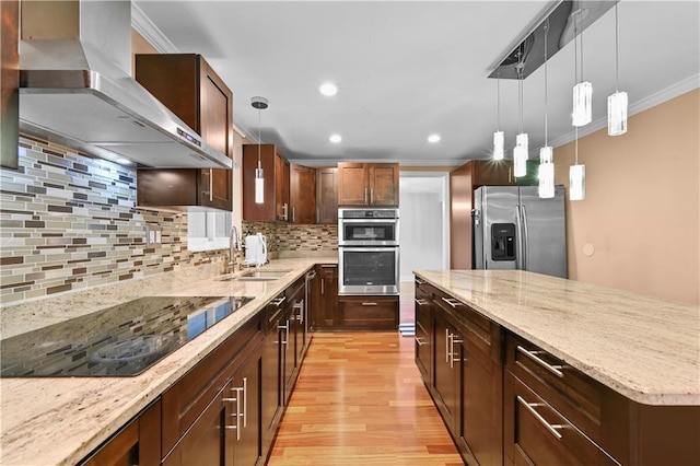 kitchen with sink, light stone counters, pendant lighting, stainless steel appliances, and wall chimney range hood