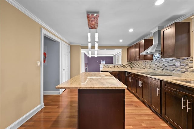 kitchen with wall chimney range hood, hanging light fixtures, black electric stovetop, light stone countertops, and a kitchen island