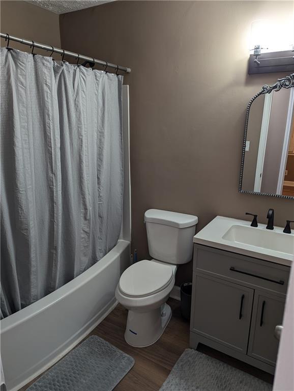 full bathroom featuring hardwood / wood-style floors, shower / bath combination with curtain, vanity, toilet, and a textured ceiling