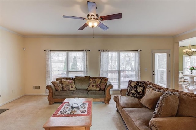 living room featuring crown molding, ceiling fan with notable chandelier, a healthy amount of sunlight, and light carpet