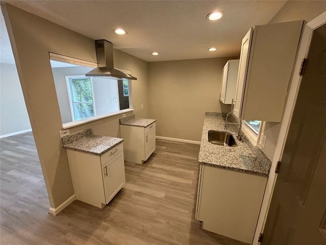 kitchen featuring white cabinets, light wood-type flooring, sink, light stone counters, and ventilation hood