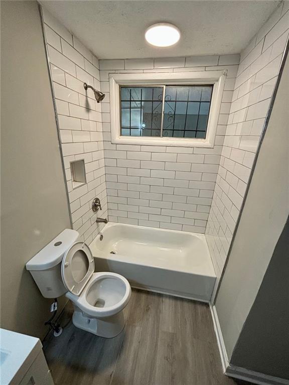 bathroom featuring toilet, tiled shower / bath combo, hardwood / wood-style flooring, and a textured ceiling