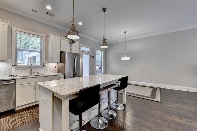 kitchen with stainless steel appliances, a sink, crown molding, a center island, and dark wood-style floors