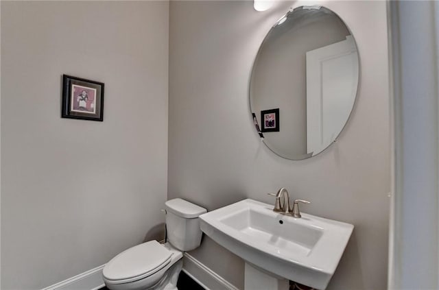 half bath with toilet, a sink, and baseboards