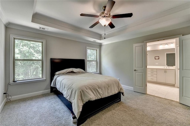 bedroom with a tray ceiling, light colored carpet, ornamental molding, baseboards, and ensuite bath