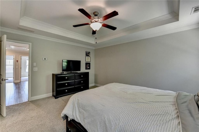 carpeted bedroom with a raised ceiling, attic access, crown molding, baseboards, and ceiling fan