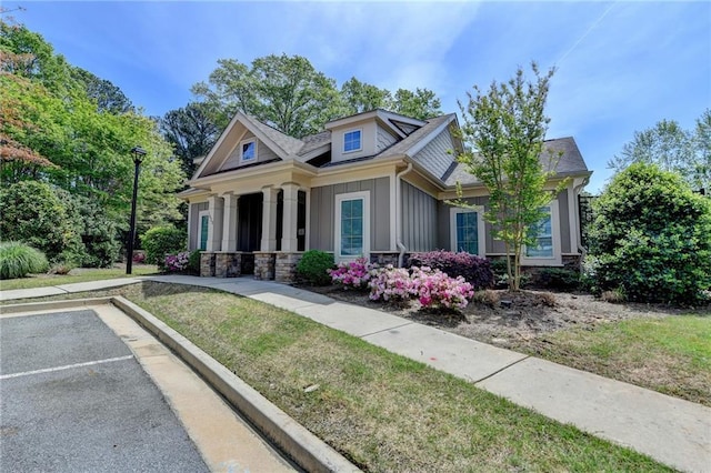 view of front facade featuring board and batten siding, stone siding, uncovered parking, and a front yard