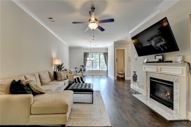 living area featuring crown molding, dark wood-style flooring, ceiling fan, a premium fireplace, and baseboards