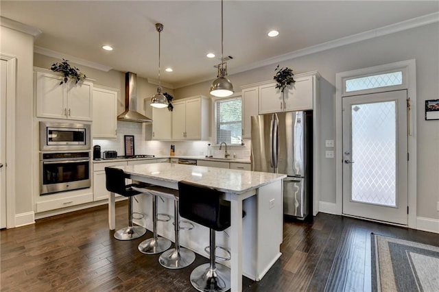 kitchen featuring stainless steel appliances, wall chimney range hood, a center island, backsplash, and light stone countertops