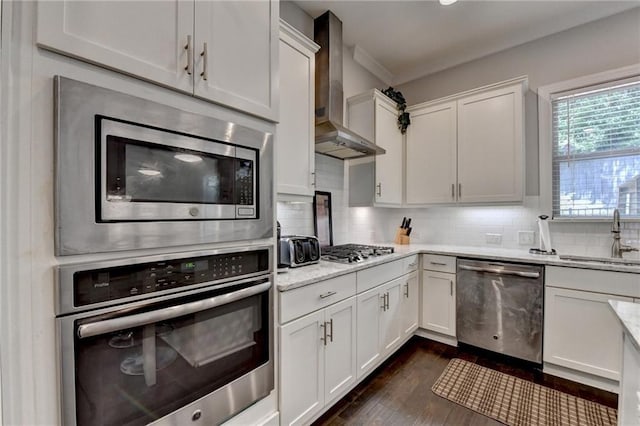 kitchen featuring stainless steel appliances, a sink, wall chimney exhaust hood, and white cabinets