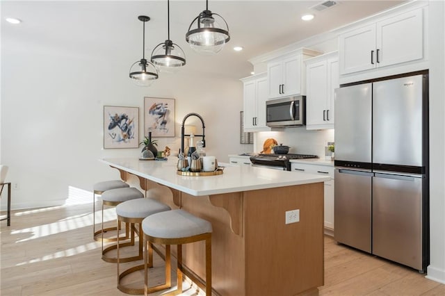 kitchen featuring white cabinets, appliances with stainless steel finishes, light countertops, an island with sink, and light wood-type flooring