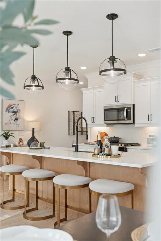 kitchen featuring pendant lighting, a kitchen breakfast bar, light countertops, stainless steel microwave, and white cabinets