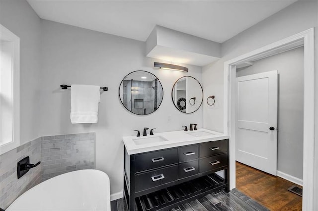 full bath with a sink, a soaking tub, wood finished floors, and double vanity