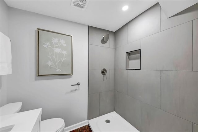 full bath featuring visible vents, toilet, a tile shower, baseboards, and vanity